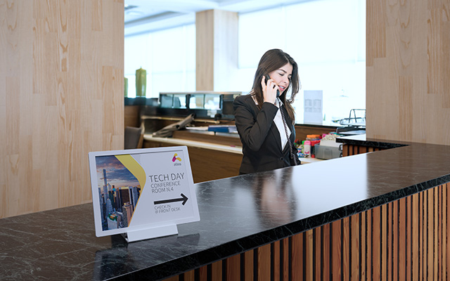 A receptionist answers the phone, signage points to an event room